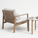 זווית אחורית של כורסת לאונג' מעוצבת MILOS לצד שולחן. ריהוט גן יוקרתי של LÜMA, שלדת אלומיניום דמוי עץ, חבל סרוג וריפוד בד אולפין.